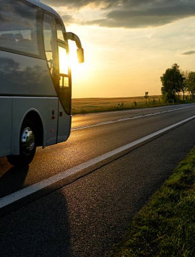 White Bus driving along the asphalt road in a rural landscape at sunset.