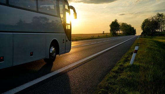 White Bus driving along the asphalt road in a rural landscape at sunset.